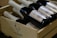 Several bottles of wine with white labels are neatly arranged inside a wooden crate. The crate features an illustration of a rooster and some branding text. The bottles are dark in color with bright labels.