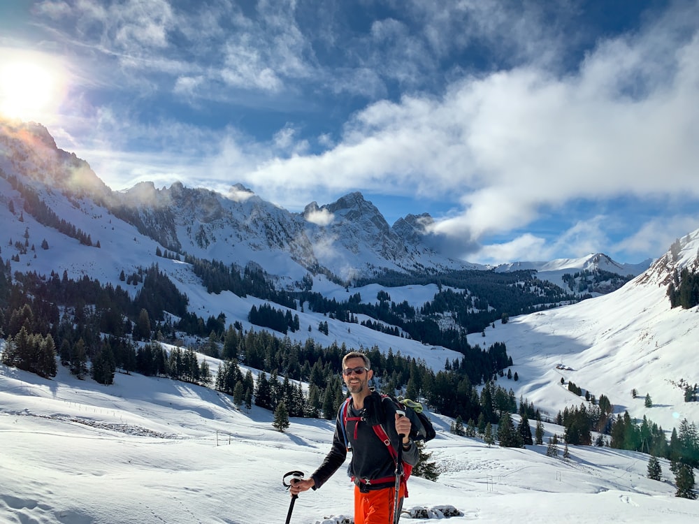 man in red jacket and blue denim jeans standing on snow covered ground during daytime