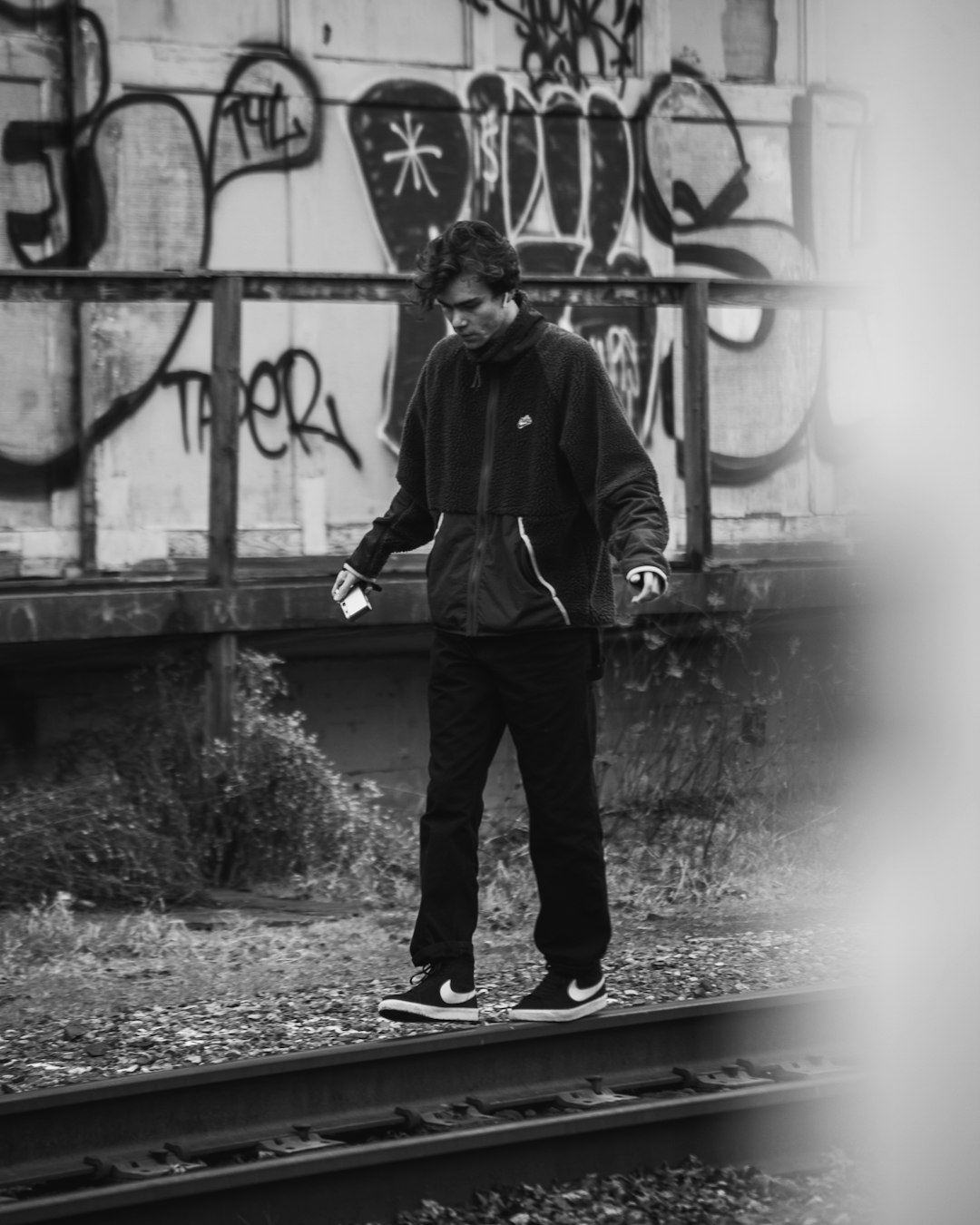 man in black jacket and pants standing beside graffiti wall