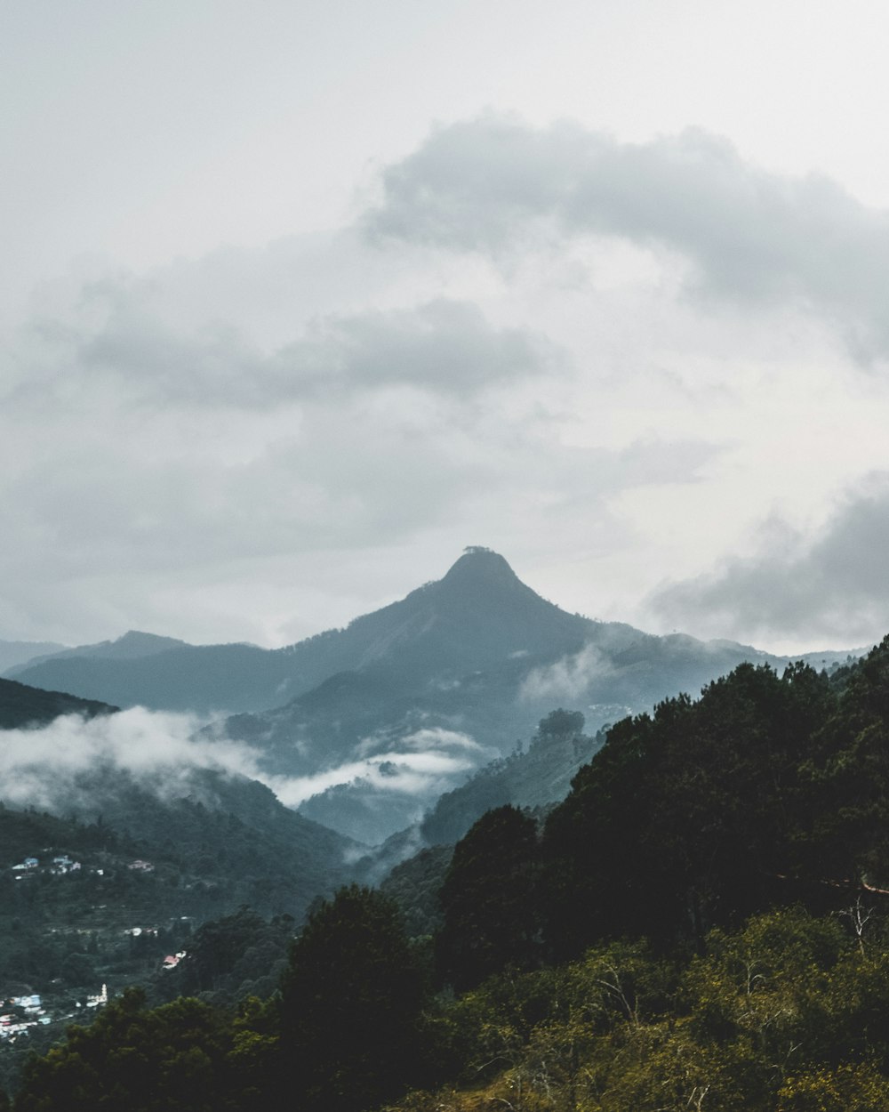 green trees near mountain under white clouds during daytime