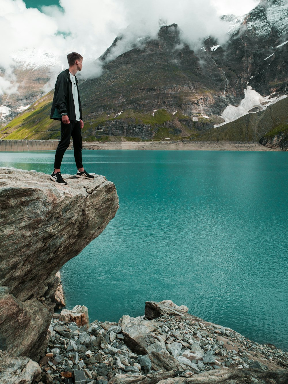 man in black pants standing on rock near body of water during daytime
