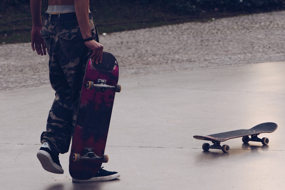 man in green and brown camouflage pants and black shoes holding black skateboard