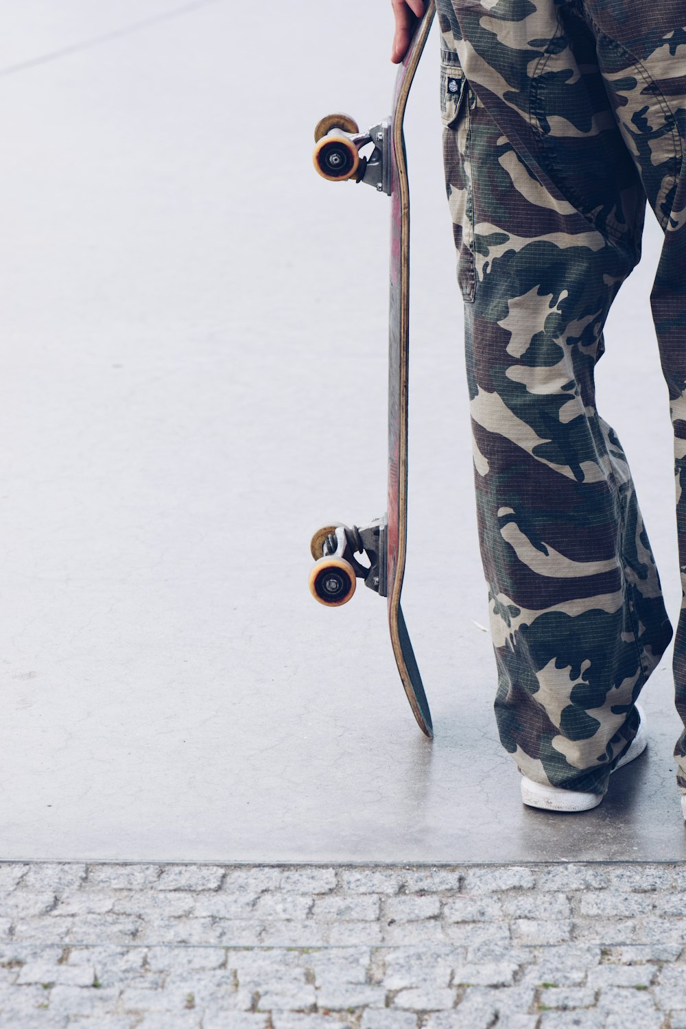 person in green black and white camouflage pants and black shoes holding brown stick