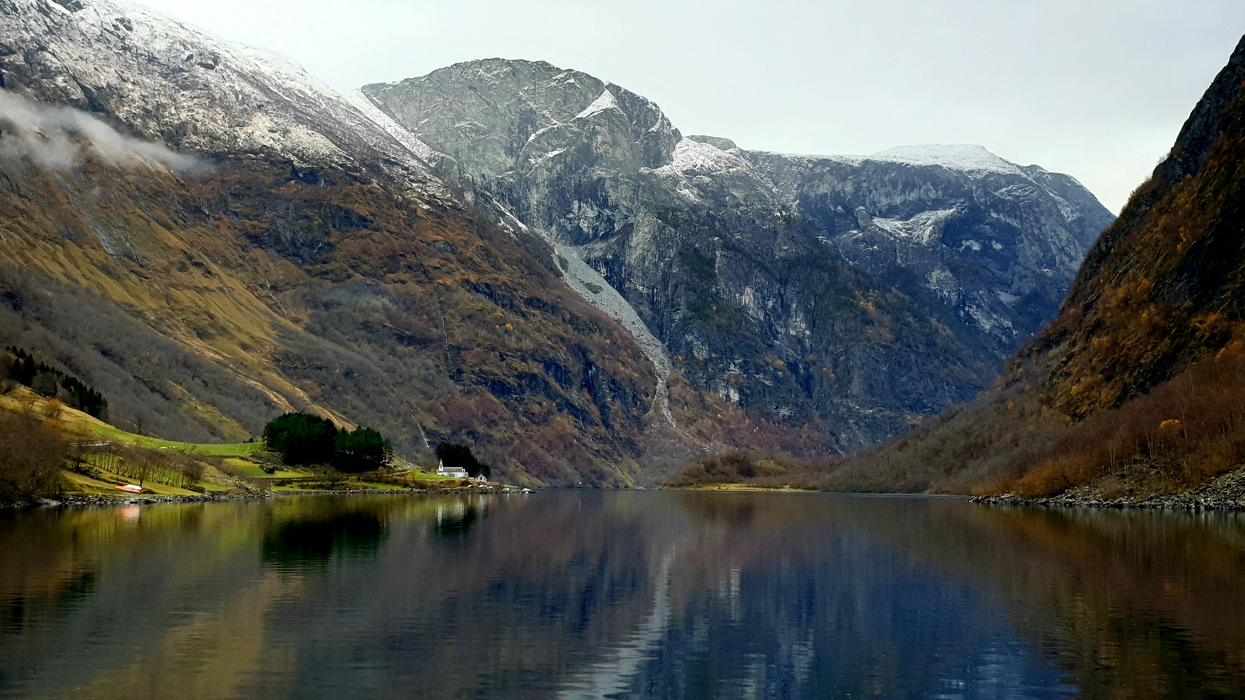 lake near mountain under white sky during daytime