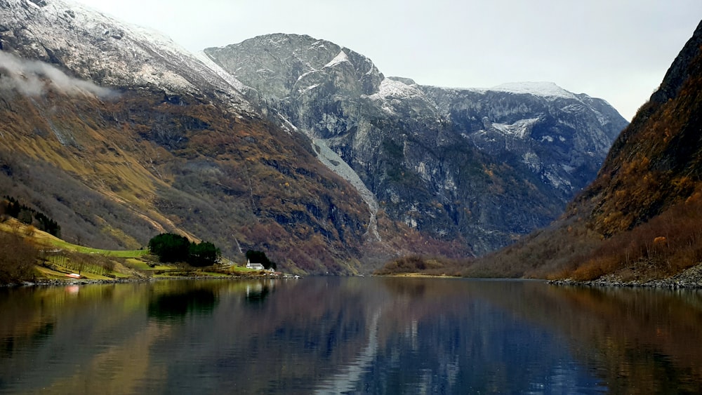 lake near mountain under white sky during daytime