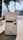 A vintage computer tower with a beige color, featuring a floppy disk drive, CD drive, and multiple buttons, placed outdoors on a sunlit sidewalk. The background includes blurred elements of greenery and parked cars.