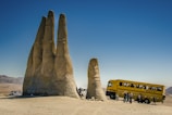 people sitting on brown sand near yellow bus during daytime