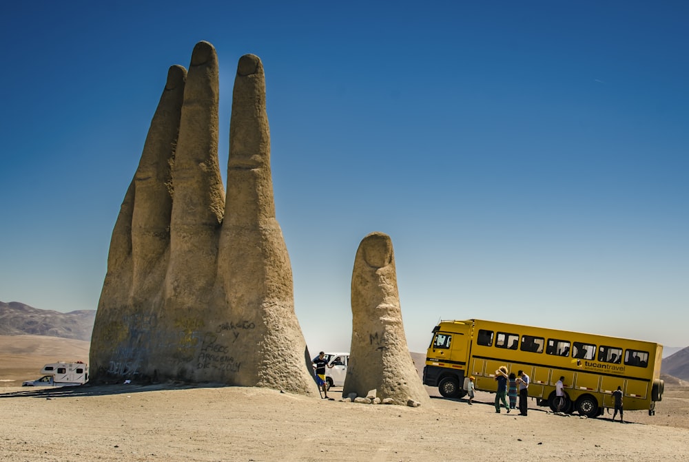 昼間、黄色いバスの近くの茶色の砂浜に座っている人々