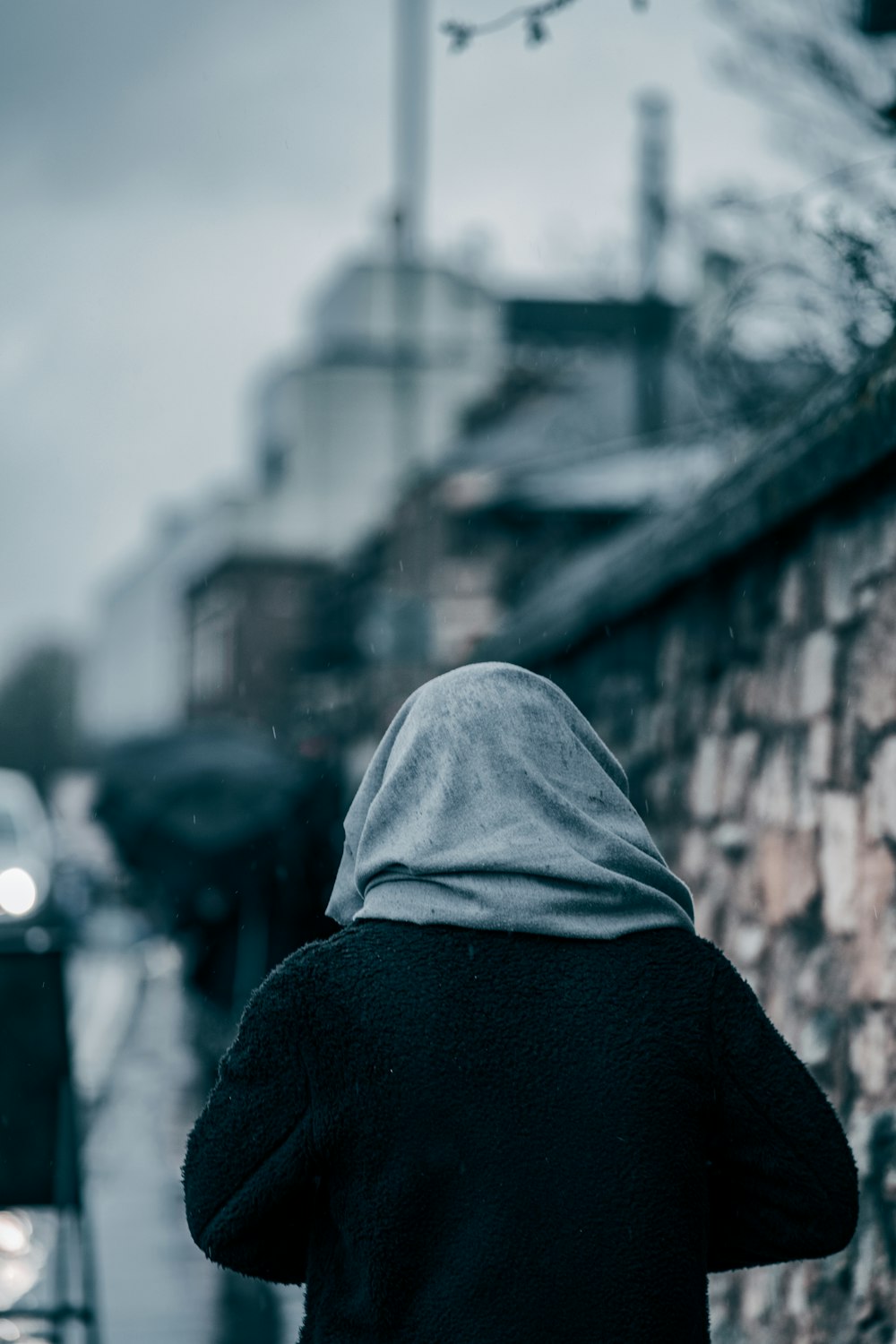 person in black hoodie standing near brick wall