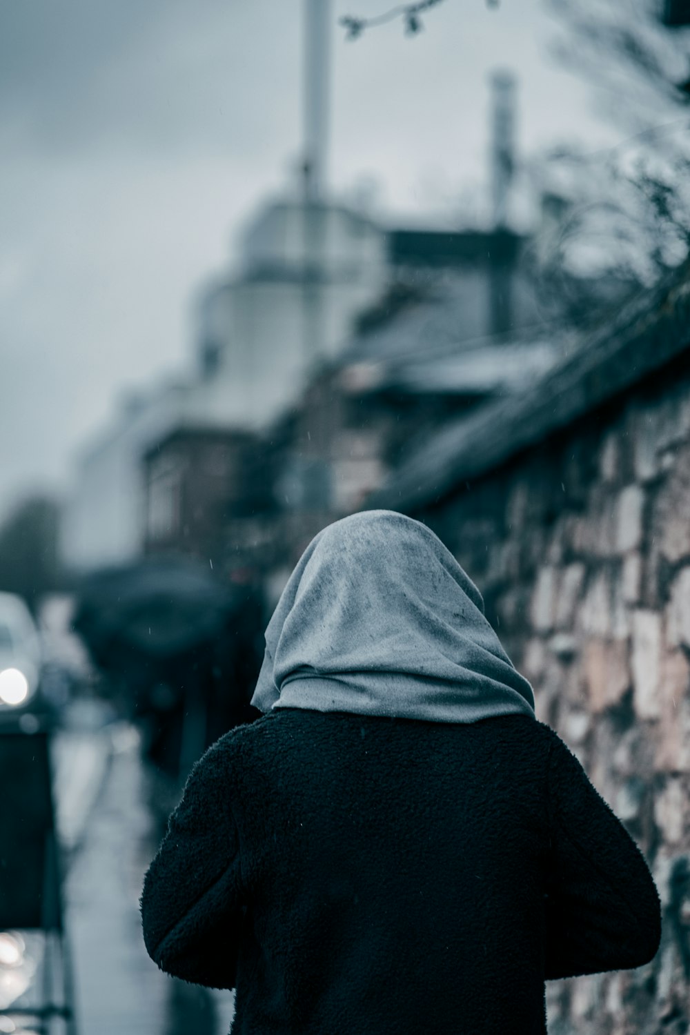 Persona con sudadera con capucha negra de pie cerca de la pared de ladrillo