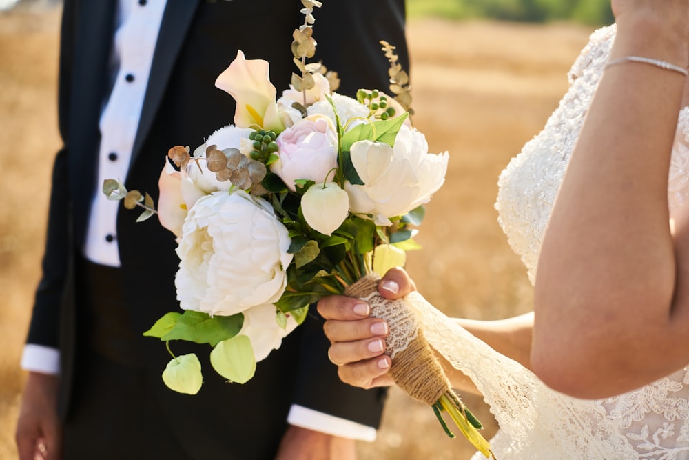 man in black suit holding white flower bouquet