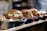 A row of delicious pulled pork sandwiches with macaroni and cheese, served in small black trays. The sandwiches have a glossy bun and are garnished with purple cabbage and lettuce.