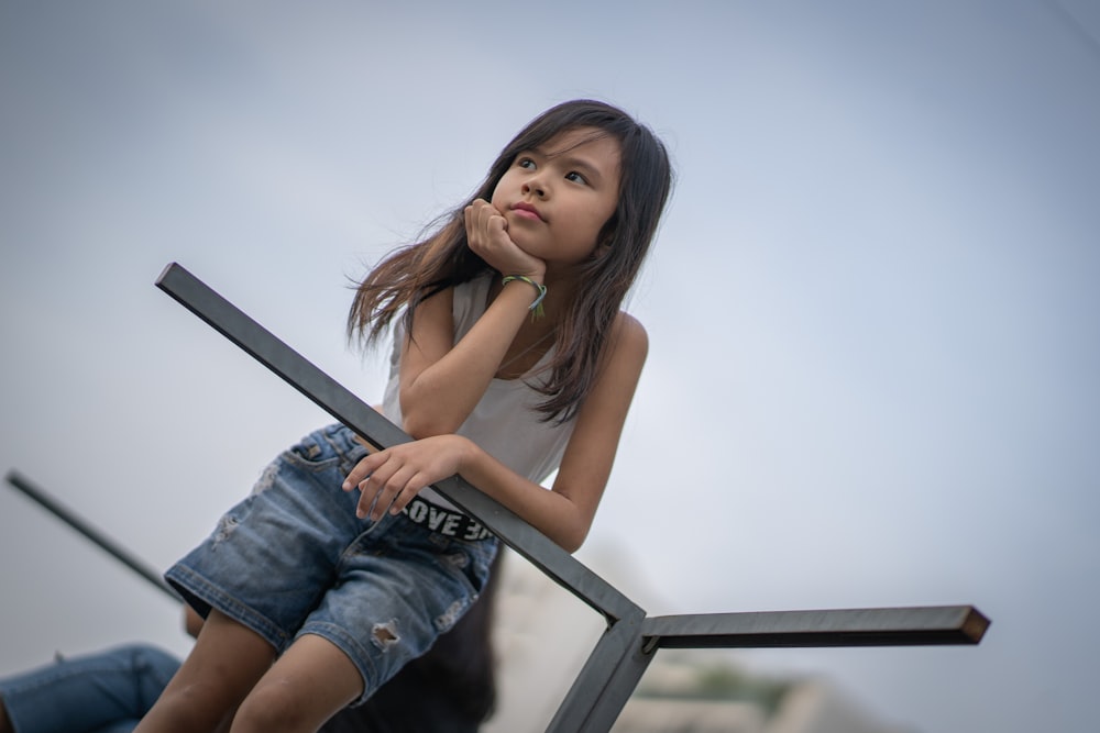 woman in blue denim shorts sitting on black metal railings during daytime