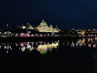 A modern commercial building illuminated at dusk reflecting on a calm river.