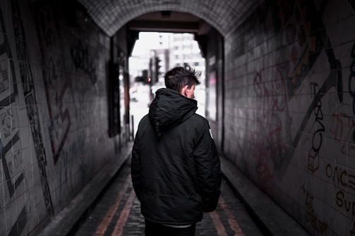 A person walking down a graffiti-covered alley wearing a hoodie and joggers.