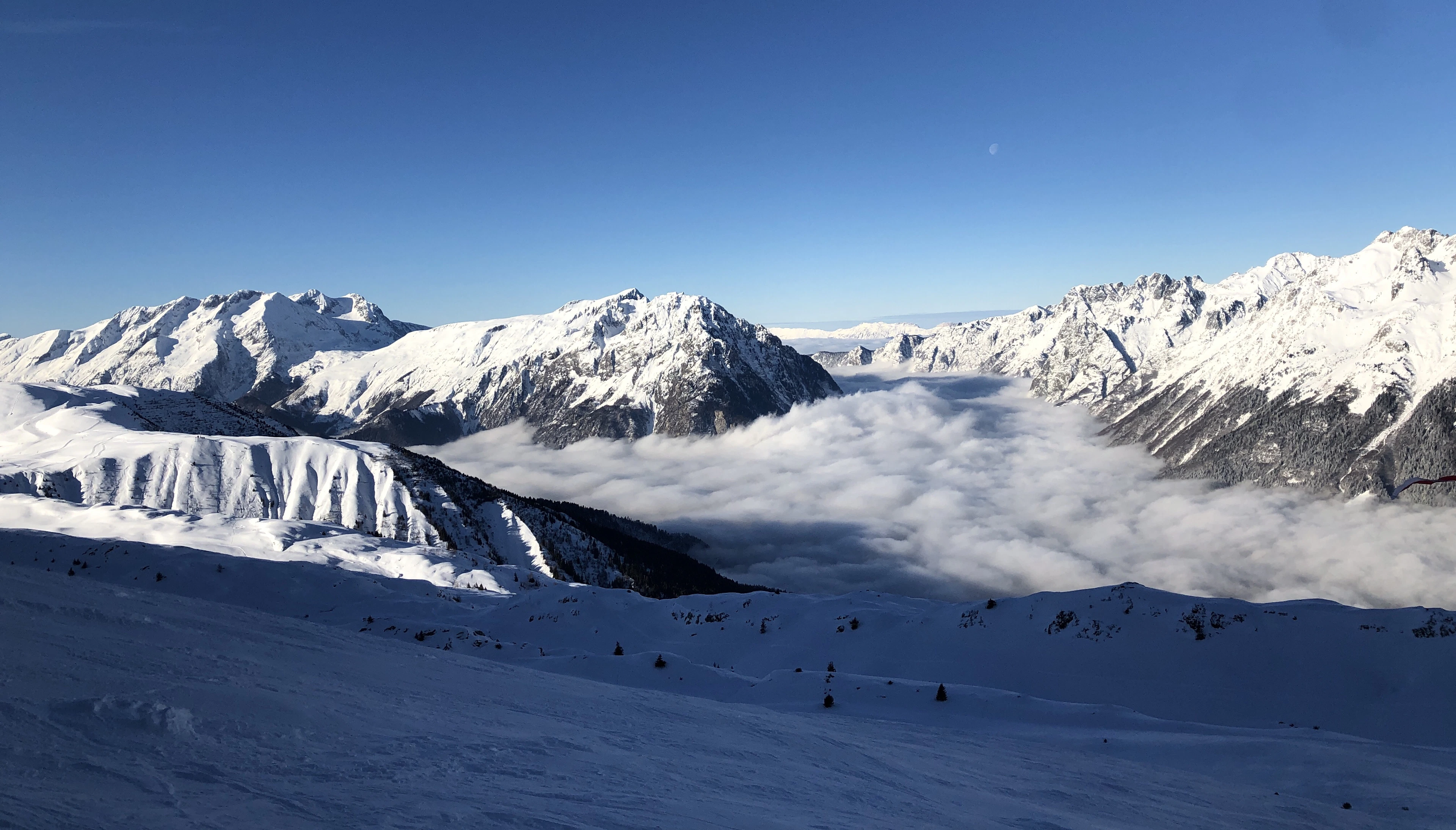 A wide snowy slope above a valley filled with cloud at Alpe d'Huez, with white ridges on both sides under a blue sky
