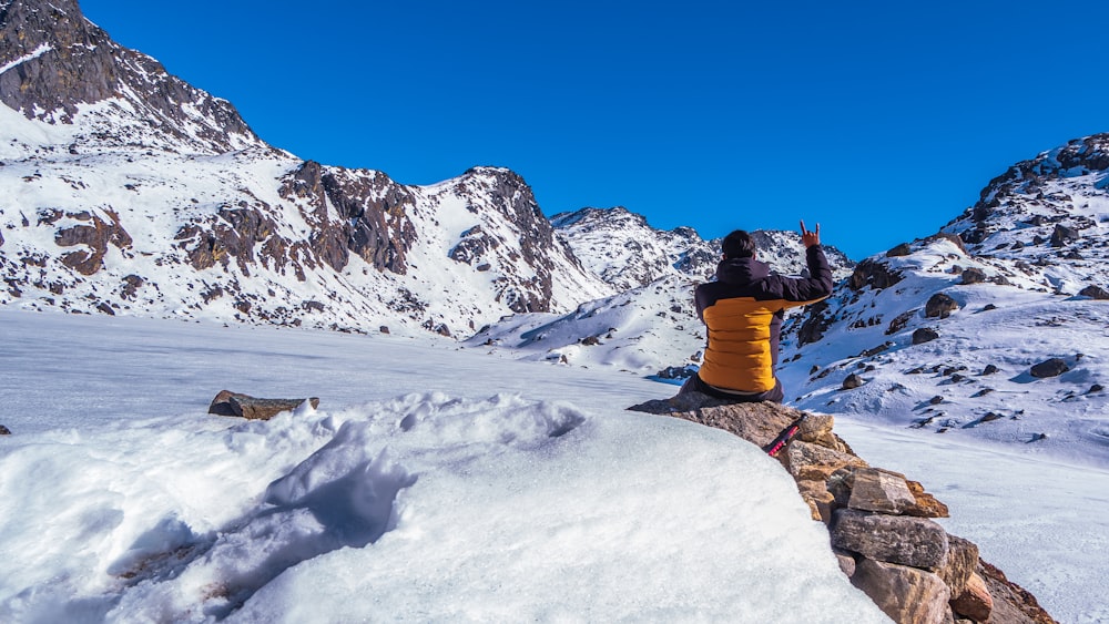 person in blue jacket and orange pants sitting on rock formation covered with snow during daytime