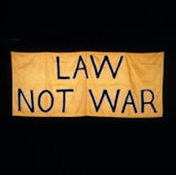 A large yellow fabric banner with bold black letters displaying the message 'LAW NOT WAR' against a dark background.
