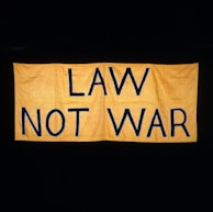 A large yellow fabric banner with bold black letters displaying the message 'LAW NOT WAR' against a dark background.