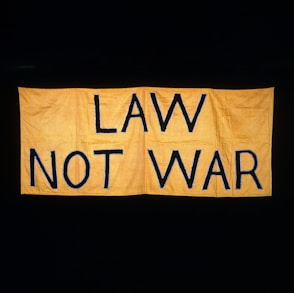 A large yellow fabric banner with bold black letters displaying the message 'LAW NOT WAR' against a dark background.