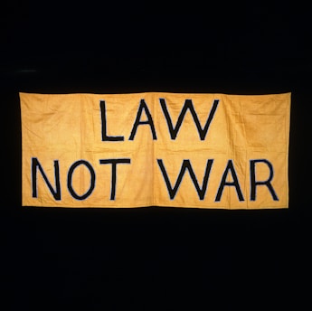 A large yellow fabric banner with bold black letters displaying the message 'LAW NOT WAR' against a dark background.