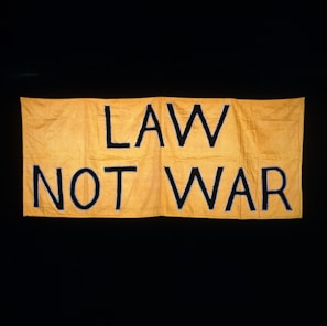 A large yellow fabric banner with bold black letters displaying the message 'LAW NOT WAR' against a dark background.