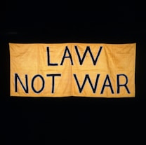 A large yellow fabric banner with bold black letters displaying the message 'LAW NOT WAR' against a dark background.