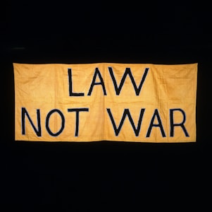 A large yellow fabric banner with bold black letters displaying the message 'LAW NOT WAR' against a dark background.