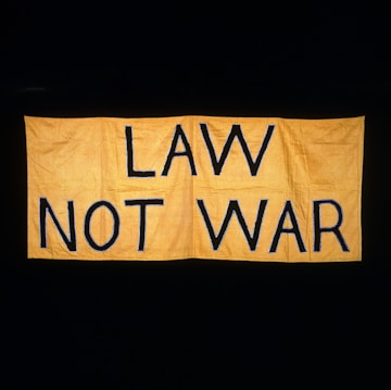 A large yellow fabric banner with bold black letters displaying the message 'LAW NOT WAR' against a dark background.