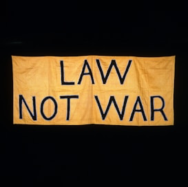 A large yellow fabric banner with bold black letters displaying the message 'LAW NOT WAR' against a dark background.