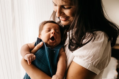 A messy bun crowned head of a mom laughing while holding her sleepy baby wrapped in a warm blanket.