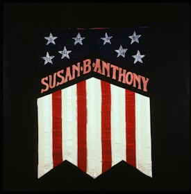 A banner featuring stars and stripes with the name 'Susan B Anthony' prominently displayed. The top section is decorated with white stars on a blue background. Below, vertical red and white stripes complete the design.