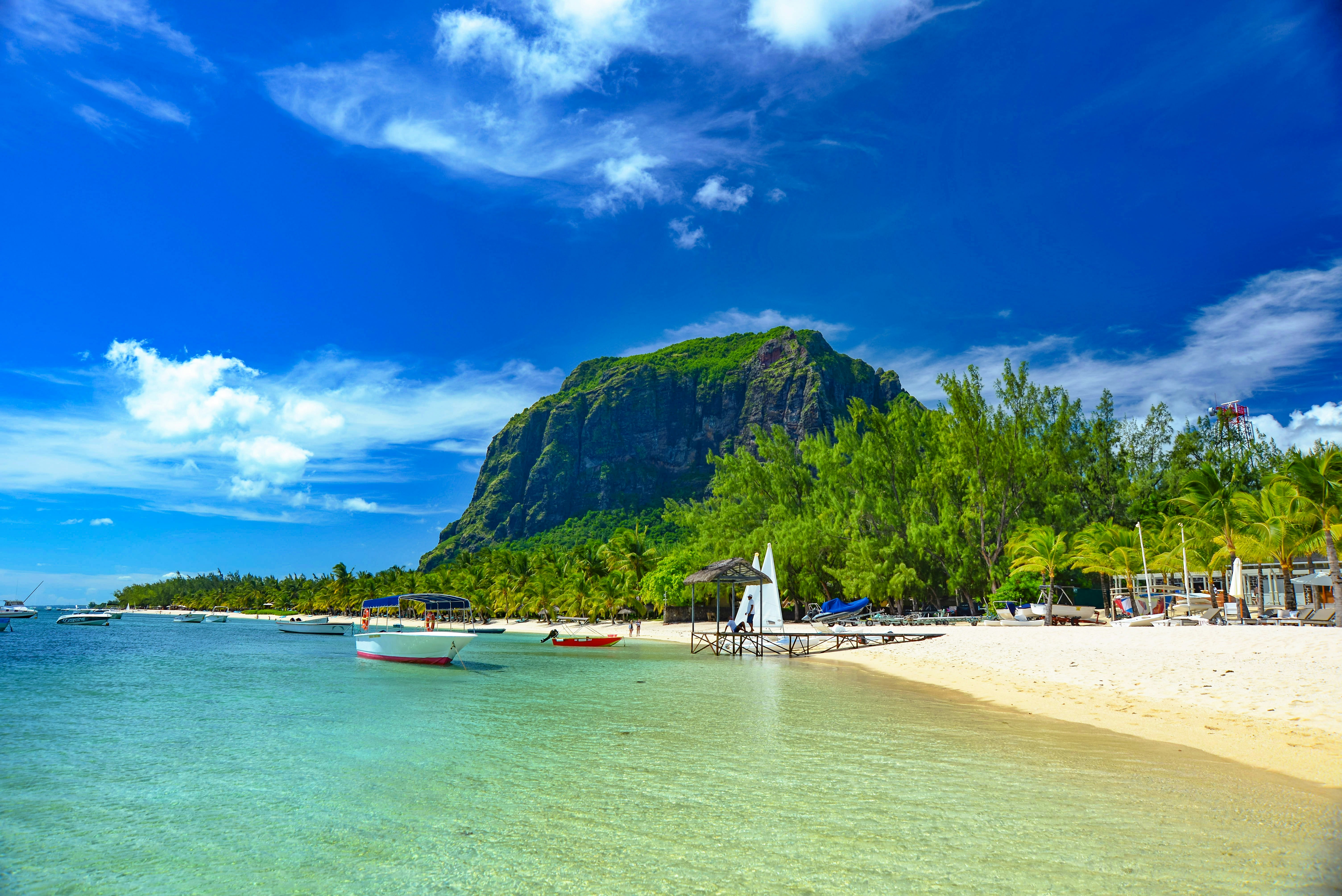 boats on sea shore near green mountain under blue sky during daytime