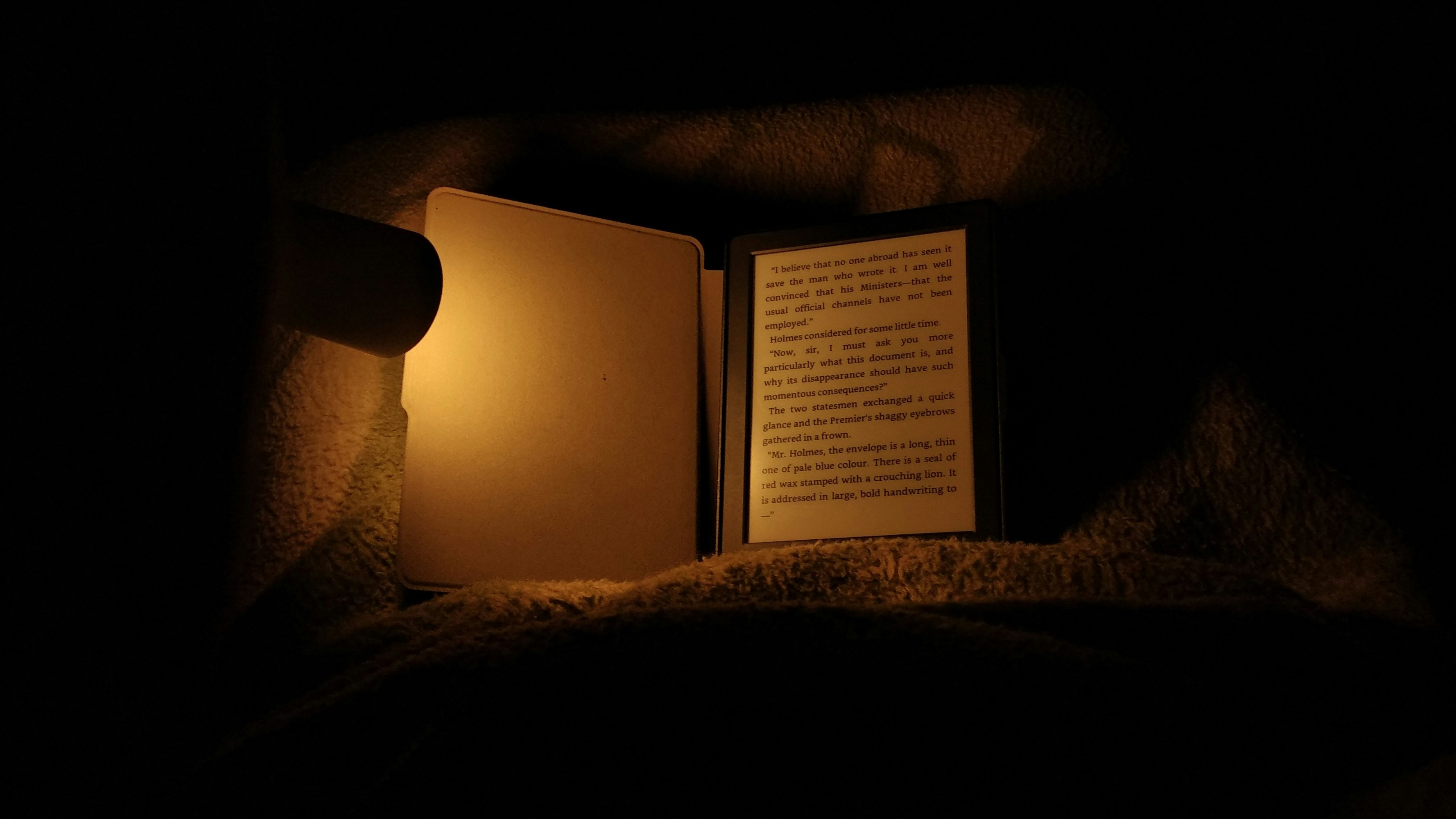 E-reader device on dark textured surface with soft warm atmospheric lighting