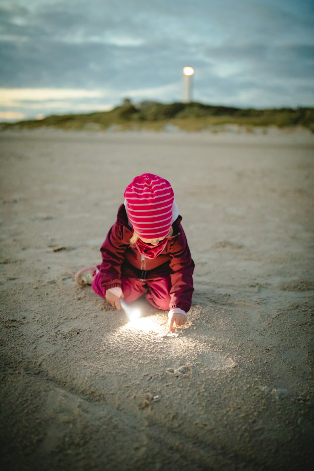 niño con sudadera con capucha roja y negra jugando en la orilla de la playa durante el día