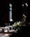 A dimly lit dining table is elegantly arranged with a centerpiece of white and green flowers. The table is set with crystal clear glasses, folded napkins, and ornate silver candle holders, creating a sophisticated and intimate atmosphere.
