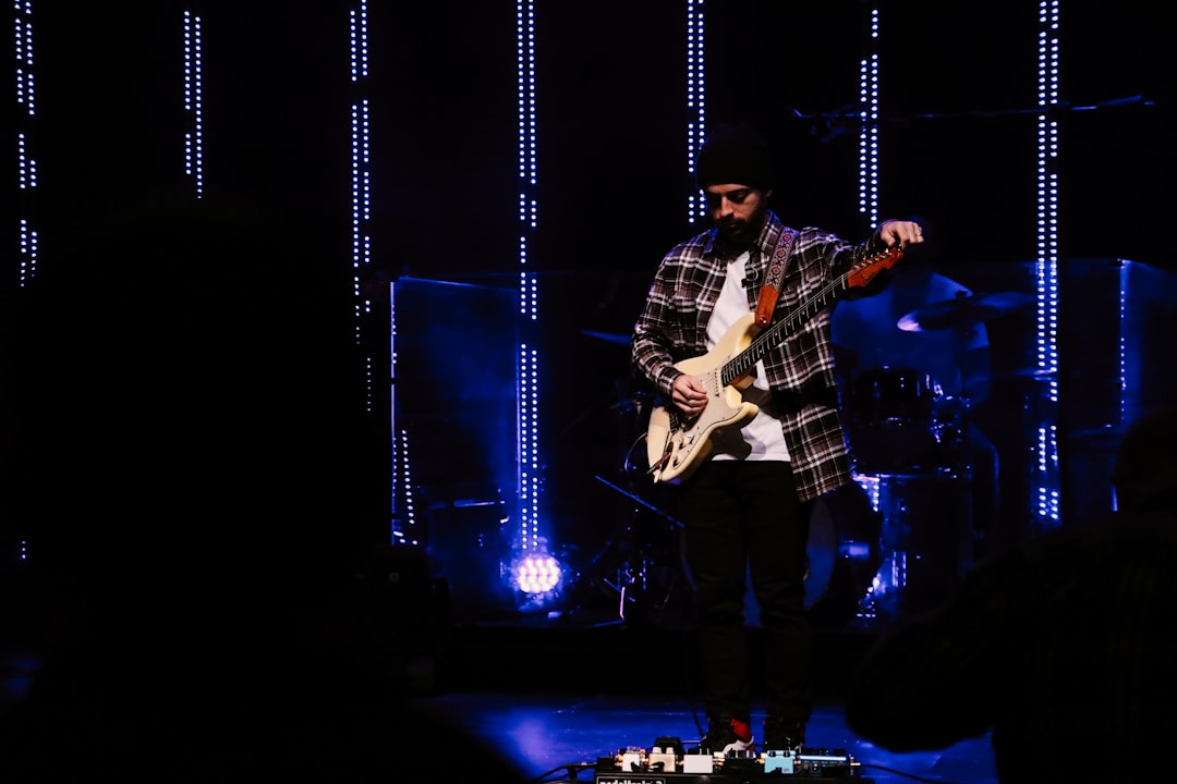 man in blue and white plaid dress shirt playing electric guitar on stage