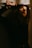 Light casts dramatic shadows across a person's face, highlighting their upward gaze and creating an atmospheric scene. The setting is dimly lit, with a warm tone emphasizing introspection and contemplation.