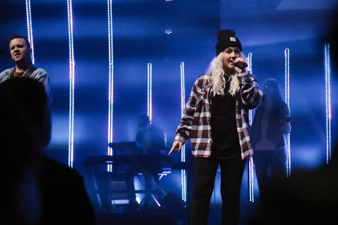 man in black and white plaid dress shirt singing on stage