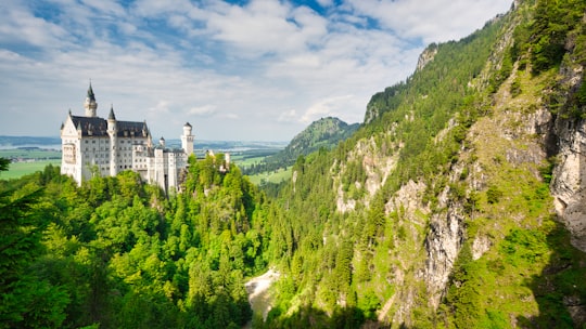 white and gray concrete building on top of green mountain under blue sky during daytime in Bavaria Germany