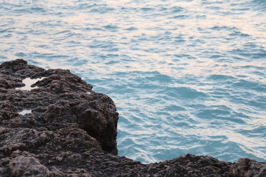 black rock formation near body of water during daytime in Kish Iran