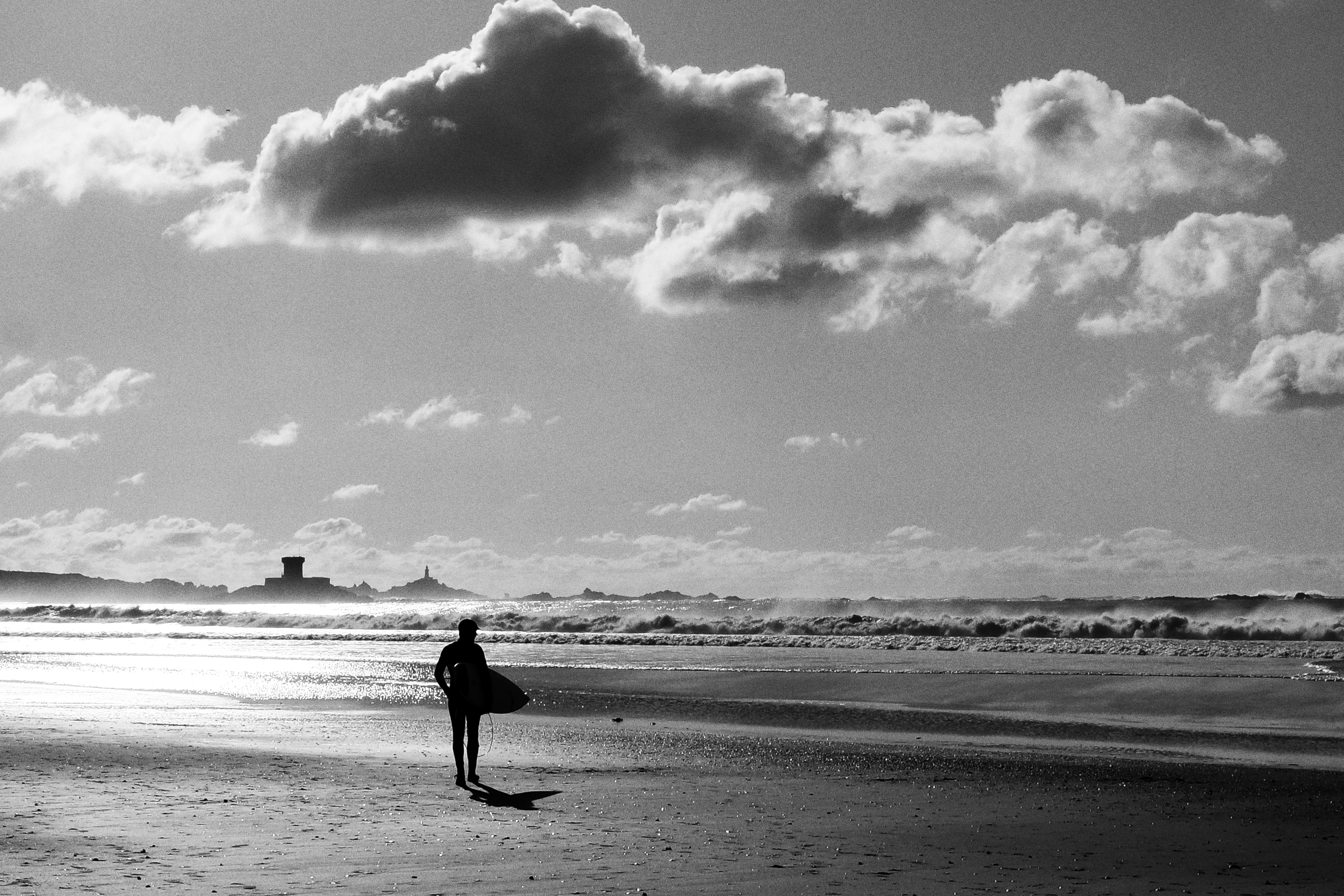 Graustufenfoto eines Mannes, der am Strand spazieren geht