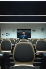 man in blue suit standing in front of brown chairs