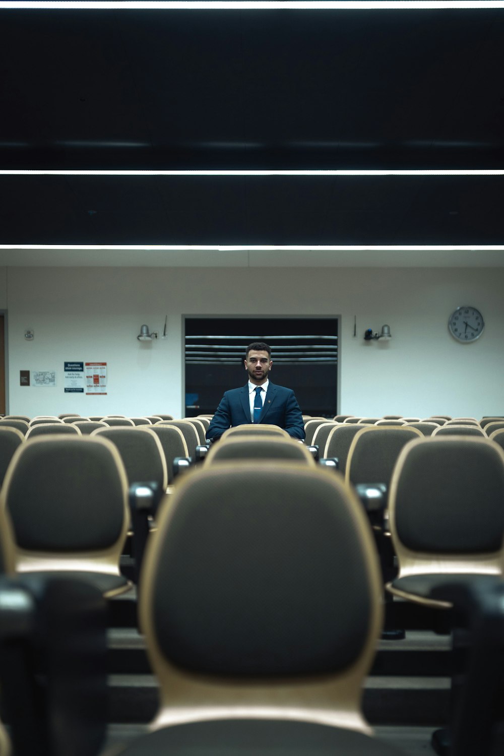 man in blue suit standing in front of brown chairs