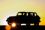 A dark, moody shot of a rugged off-road vehicle kicking up dust on a narrow mountain trail at sunset.