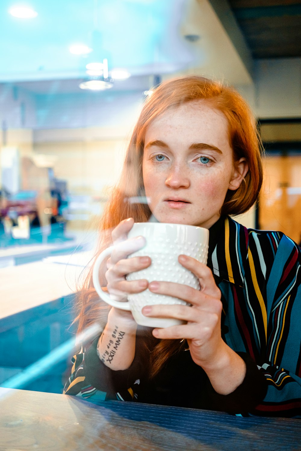woman in blue and white striped shirt drinking from white ceramic mug