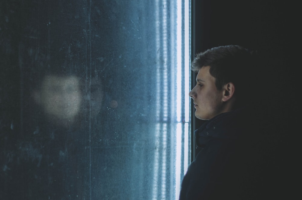 man in black hoodie standing beside blue wall