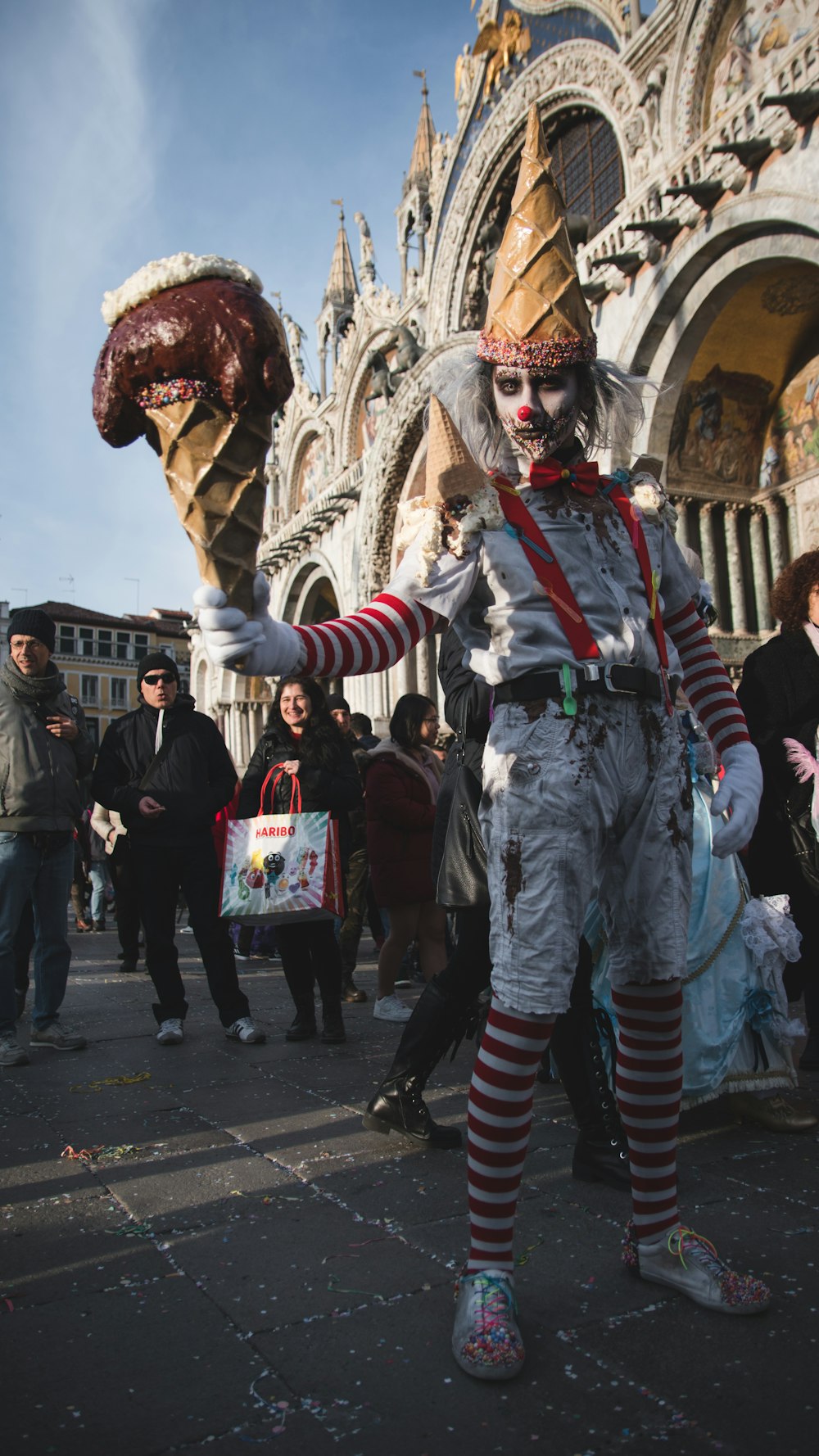 person in white and red mask holding gold mask