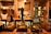 A row of traditional beer taps is lined up on a wooden bar inside a cozy pub setting, with various types of beer and ale bottles displayed on shelves in the background. Warm lighting creates a rustic and inviting atmosphere.