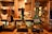 A row of traditional beer taps is lined up on a wooden bar inside a cozy pub setting, with various types of beer and ale bottles displayed on shelves in the background. Warm lighting creates a rustic and inviting atmosphere.
